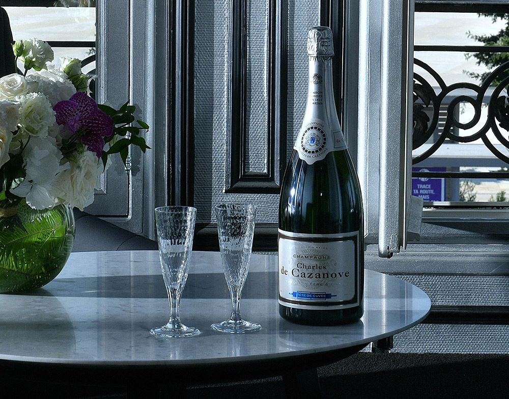 Magnum Tête de Cuvée posé sur table basse, deux flûtes et bouquet de fleurs. / Magnum Tête de Cuvée on a coffee table, two flutes and a bouquet of flowers.
