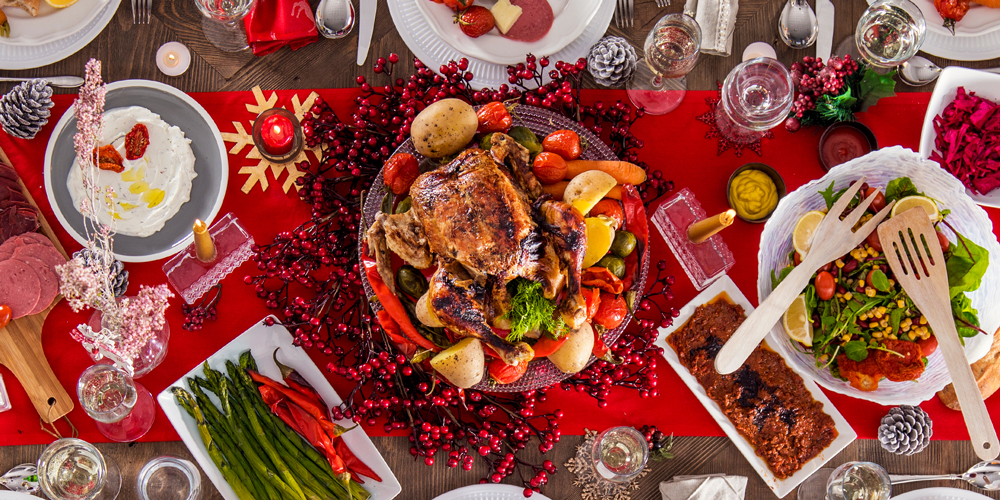 Table de fêtes de fin d’année avec au centre une dinde, d’autres plats tels que des asperges, de la burrata, chemin de table rouge, bougies / A festive table with a turkey in the centre, other dishes such as asparagus and burrata, a red table runner and candles.