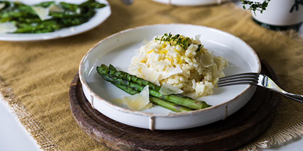 Risotto aux asperges et copeaux de parmesan dans un assiette blanche sur une table en bois / Risotto with asparagus and parmesan shavings on a white plate on a wooden table.