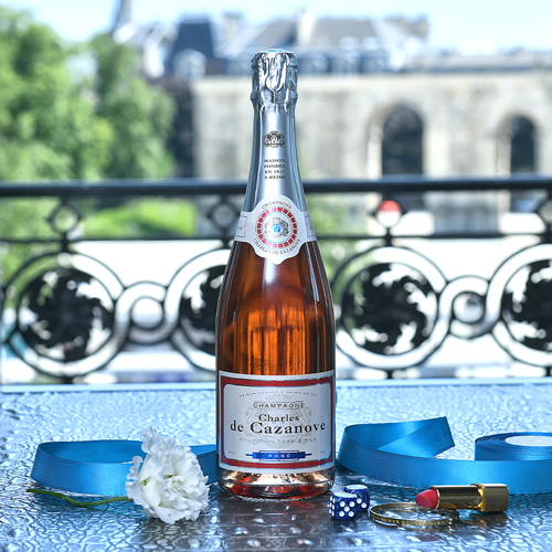 Bouteille de champagne Charles de Cazanove Rosé posée sur une table, La Porte de Mars de la ville de Reims en arrière-plan / Bottle of Charles de Cazanove Rosé champagne on a table, with the Porte de Mars in Reims in the background.